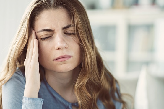 A woman closing her eyes with her hand on her temple