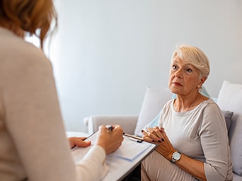 A woman sitting looking at a woman with a clipboard