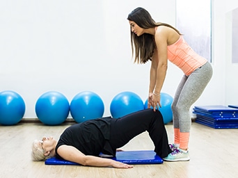 A woman doing exercises on a mat with a trainer