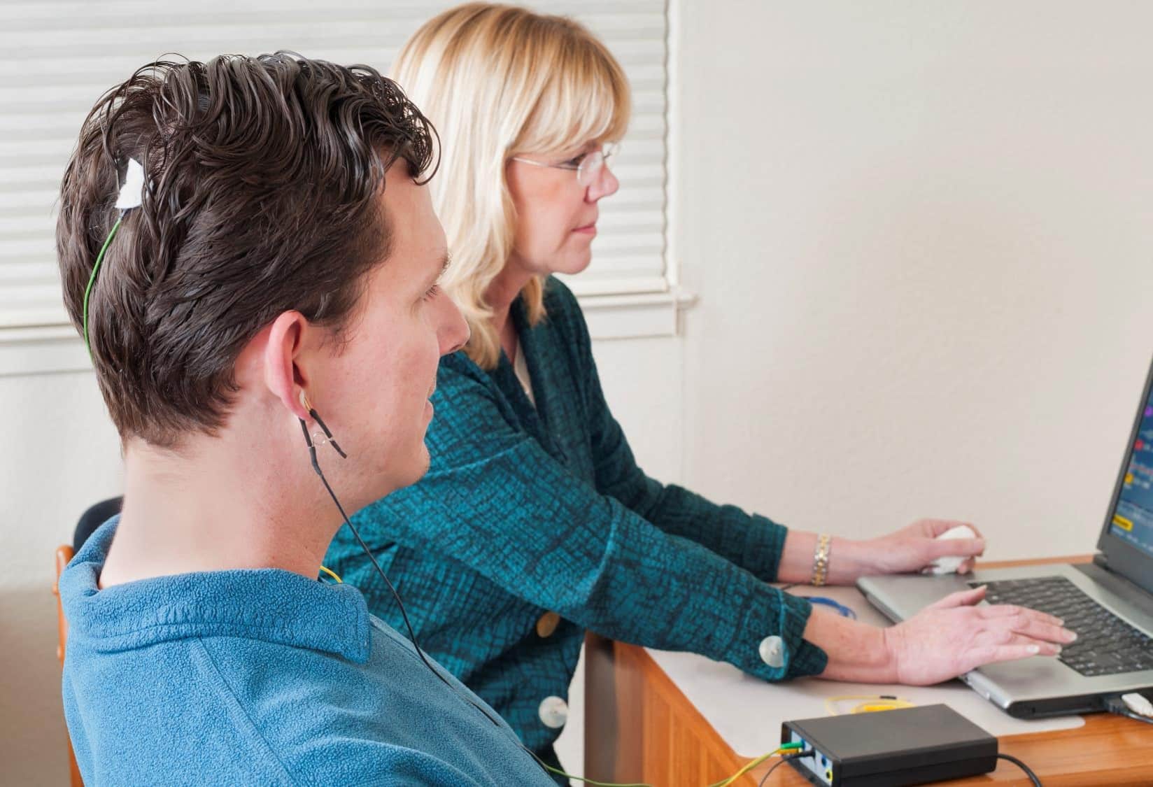 A woman sitting at a lap top next to a man with wires attached to him
